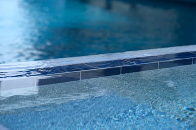 Luxurious QDI Deia Atlantic 6x6 mosaic tiles complement smooth pebble plaster finish in this sophisticated Dallas pool environment by Selah Pools.