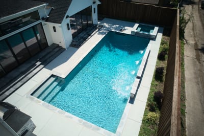 Aerial view showcasing the sophisticated interplay between raised spa and cascading water features. Burlington Quartzite coping frames the pebble plaster finish.