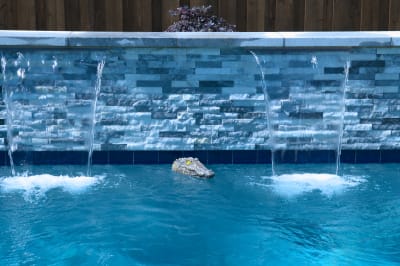 Pristine water flows through Burlington Quartzite features in this sophisticated Dallas outdoor living space, showcasing the seamless integration of natural stone with precision water elements.