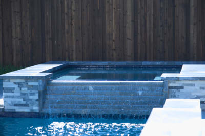 Water flows seamlessly from the raised spa across Burlington Quartzite Classico surfaces, highlighting the textural interplay between natural stone and Atlantic tile.