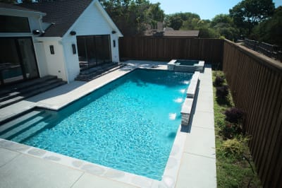 Wide exterior view showcasing the seamless integration of Burlington quartzite raised beam with smooth pebble plaster finish in this Dallas custom pool environment.
