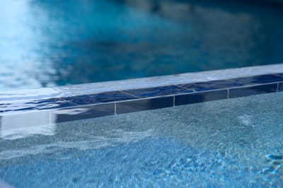 Precision-crafted Burlington Quartzite water feature beam showcases seamless sheer descent integration. The natural stone's texture creates beautiful water patterns while maintaining the clean lines essential to luxury pool design.
