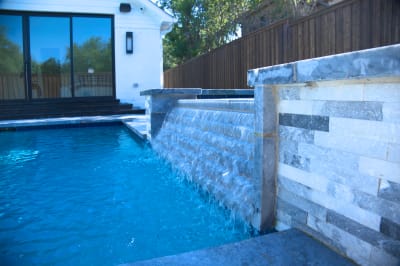Natural stone patterns emerge beneath cascading water on Burlington Quartzite Classico. The interplay of texture and flow creates visual depth in this Dallas luxury pool design.