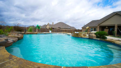 Aerial view of a family resort pool with tiered spillovers, 40-foot weeping wall, rock grotto, and custom spa built with Luder stone veneer in Haslet, Tarrant County, TX.