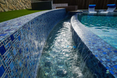 Elevated view of a blue glass tile pool with cascading water features integrated into the architectural hardscape of an Irving, Dallas County, TX estate.