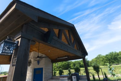 Side elevation view of the covered outdoor living pavilion showcasing stone column construction and natural beam framework integrated with the pool environment.