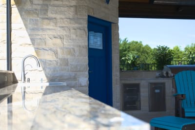 Premium granite outdoor kitchen seamlessly integrated with stone architectural elements, showcasing sophisticated material coordination in this luxury outdoor living environment.