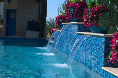 Architectural precision meets artistry in this detailed view of cascading water over Elysium Peacock mosaic tiles, framed by natural granite coping.