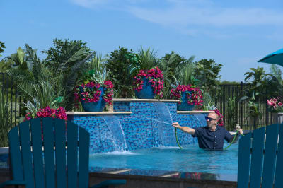 Architectural raised beam walls create stunning elevation changes while 18-inch sheer descents cascade over Elysium Peacock mosaic tile. Natural stone coping provides seamless integration with the outdoor living environment.