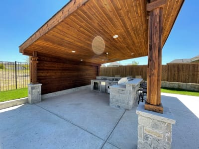 Covered outdoor living space featuring a stone fireplace with wood-clad ceiling at the Phillips residence in Roanoke, Denton County, TX.