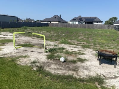 A Justin, TX backyard showcases a 15,023-gallon freeform pool with soccer goal and grill cabinet, featuring natural stone columns, twin sheer descents, and blue turtle mosaics.