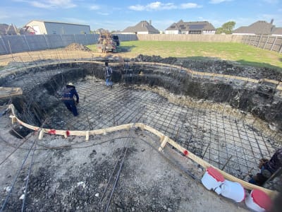 Deck-level view across travertine deck to a freeform pool with twin 12" sheer descents, showing the smooth travertine coping and raised beam wall in Justin, TX.