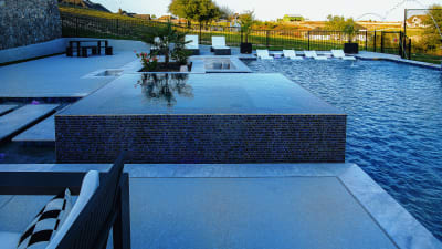 The raised spa at dusk with still, mirror-reflective water creating the "glass for water" effect, viewed from the fire pit seating area