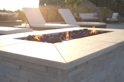 Establishing aerial overview of a contemporary geometric pool with infinity edge, sunken seating area, fire pits, laminar jets, and tile-veneered columns at a Fort Worth, TX estate.
