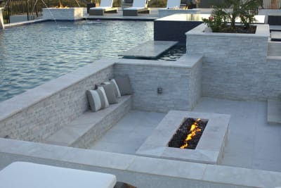 Fort Worth outdoor patio with brick wall, fire pit, and pool featuring water features, stone seating area, and illuminated trees