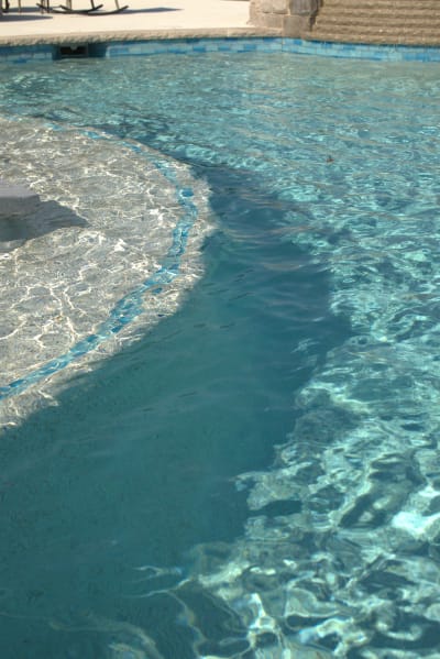 Deck-level view of Aquabella OD-2441 flat spillover tile and Spray Deck Perla decking at a freeform pool in Azle, Parker County, TX.