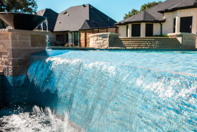 Close-detail view of the Aquabella Bora Bora 647 tile negative edge and Buff Lueders chopped stone veneer on a freeform infinity-edge pool in Granbury, Hood County, TX.