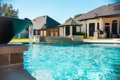 Water bowl pouring into the pool with elevated spa steps and house backdrop at the Sharp residence in Granbury, TX