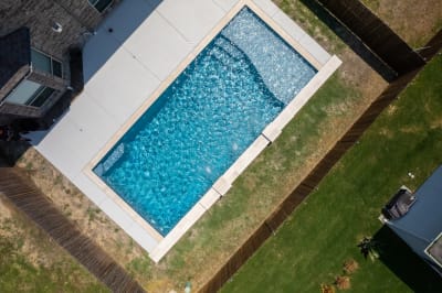 Close-up detail of Arctic White pebble plaster finish along the waterline of a geometric pool with NPT Parallax PLL Blue glass tile in North Richland Hills, TX.
