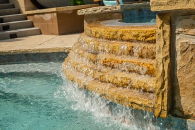 Close-detail view of water cascading from a stone fountain feature into the tile-lined pool at a Flower Mound, Denton County, TX residence crafted through Selah's collaborative Design Center process.