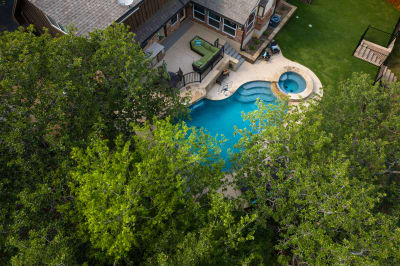 Aerial view of an exceptional Flower Mound, TX outdoor living space featuring a custom pool with sleek Lautner edges and a vibrant blue tile sunshelf.