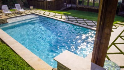 Hero view of a family resort pool in Irving, Dallas County, TX, featuring love seats, a cascading waterfall, weeping walls, and travertine coping over a pebble finish interior.