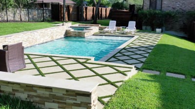 Weeping walls cascade over stone veneer spa tile into a plaster and quartz pool with travertine and granite deck surrounds in Irving, TX.