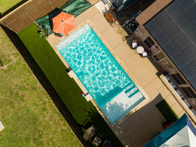 Establishing overview of a geometric custom pool with six-tiered spa spillover, Buff Lueders stone veneer columns, and Ultra Blue plaster finish in Arlington, TX.