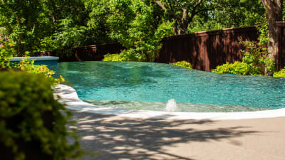 Raised spa with travertine ledgestone veneer and cascading spillway flowing into a 9,001-gallon infinity-edge pool with Burlington Milano White coping in Grapevine, TX.