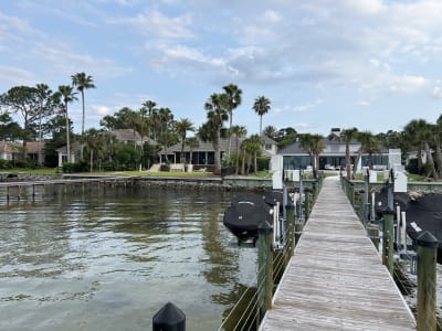 Waterfront dock with boats and palm trees at a luxury Miramar Beach, FL residence with landscaped lawn and blue skies.