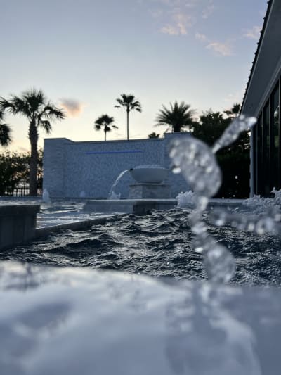 Luxury pool with water features spraying at sunset, palm trees backdrop, Sheldon Residence, Miramar Beach, FL.