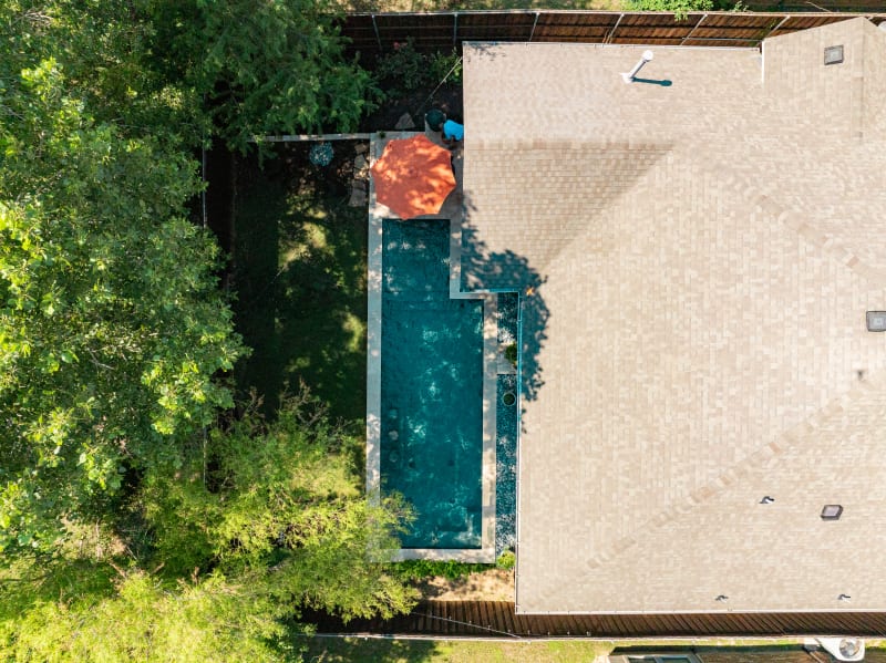 Aerial view of a contemporary geometric pool with stone veneer raised beam wall and concrete paver decking in Arlington, Tarrant County, TX.