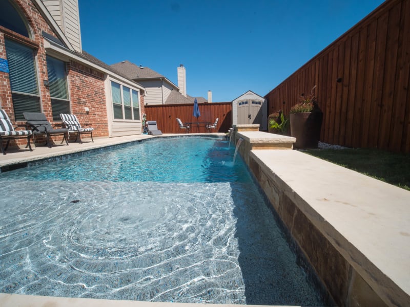 Hero view of a custom pool with a tanning ledge and brick patio deck crafted for a Dallas County residence in Grand Prairie, TX.