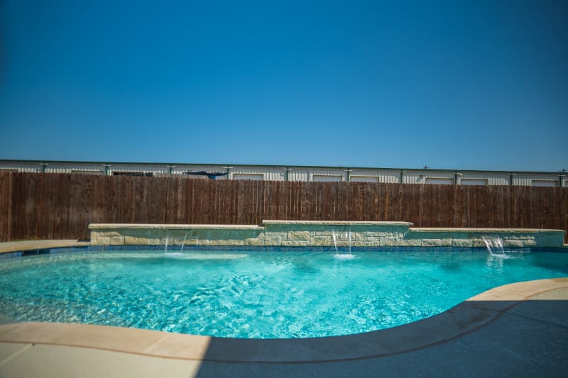 Establishing overview of a contemporary outdoor living space in Fort Worth, TX, featuring a raised spa with Buff Lueders stone veneer, flat spillover, and Arctic White pebble plaster pool.