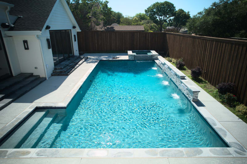 Sophisticated raised beam design creates dramatic elevation changes throughout this custom Dallas pool environment, featuring multiple sheer descent water features and Burlington quartzite coping.