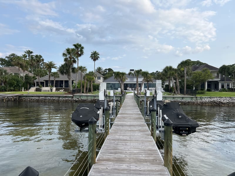 Wooden dock and boat launch at a luxury waterfront residence in Miramar Beach, FL, framed by calm water and palm trees.