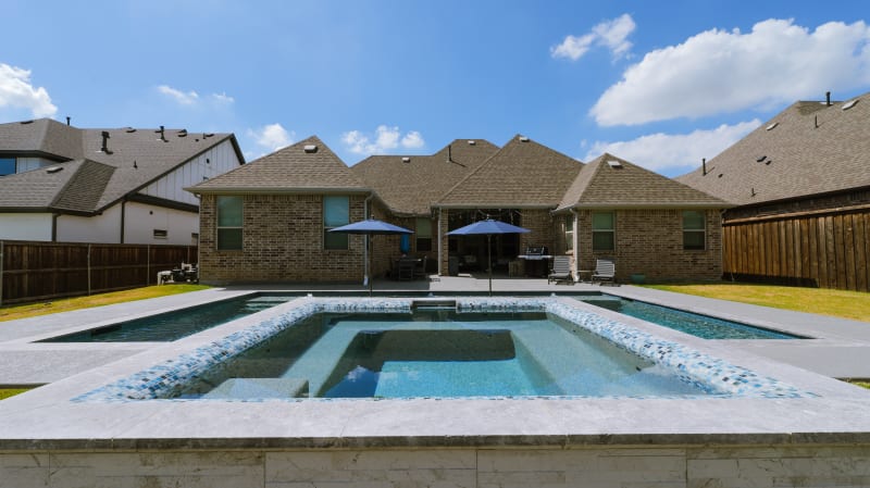 Close detail of a 36-inch sheer descent cascading over Burlington Armani Grey travertine coping into Gothic Spruce Green tile water at a North Richland Hills, TX geometric pool.