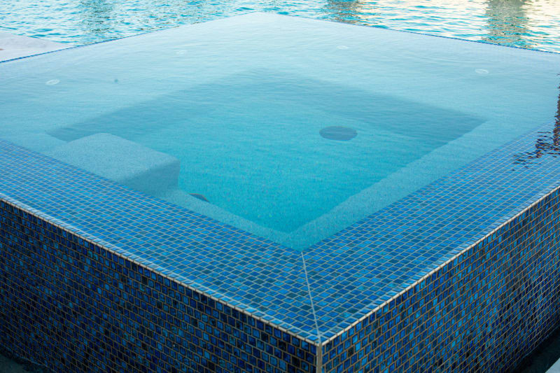 Top-down view of the raised geometric spa interior showing full blue glass mosaic tile coverage and overflow edge
