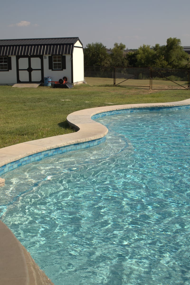 A freeform pool and oversized circular spa with tiered spillover, set against a rolling Azle landscape under the Texas sun.