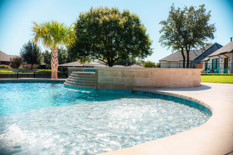 Tiered spillover cascading from the elevated spa into the freeform pool with Buff Lueders stone raised beam columns and palm tree at the Sharp residence in Granbury, TX