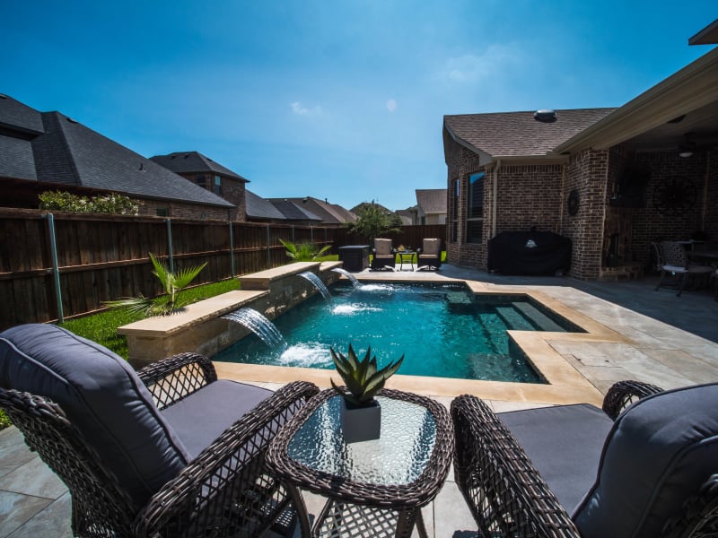 Establishing view of a custom square spa with integrated waterfall system crafted for evening relaxation at a Mansfield, Tarrant County, TX residence.