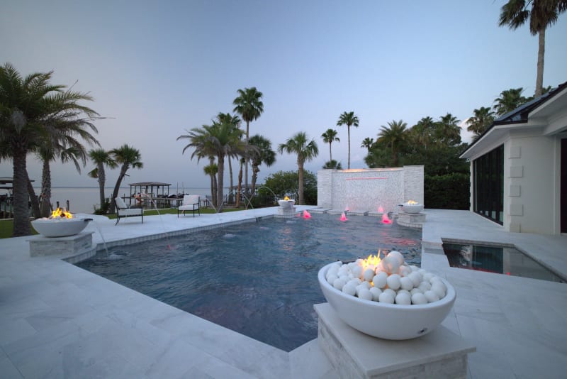 Hero view of a custom resort-style pool in Miramar Beach, FL, featuring a raised fire feature, bubblers, 8-foot linear LED waterfall, and Blue Surf plaster.