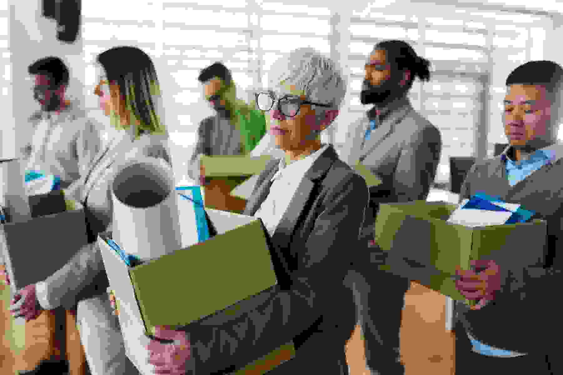 Large group of displeased business people carrying carton boxed with their belongings after being fired from their jobs.