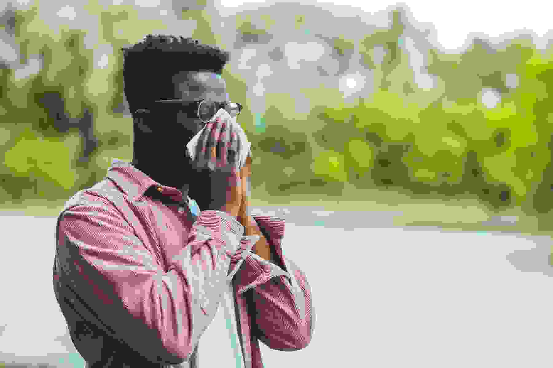A Black man blowing his nose in a park