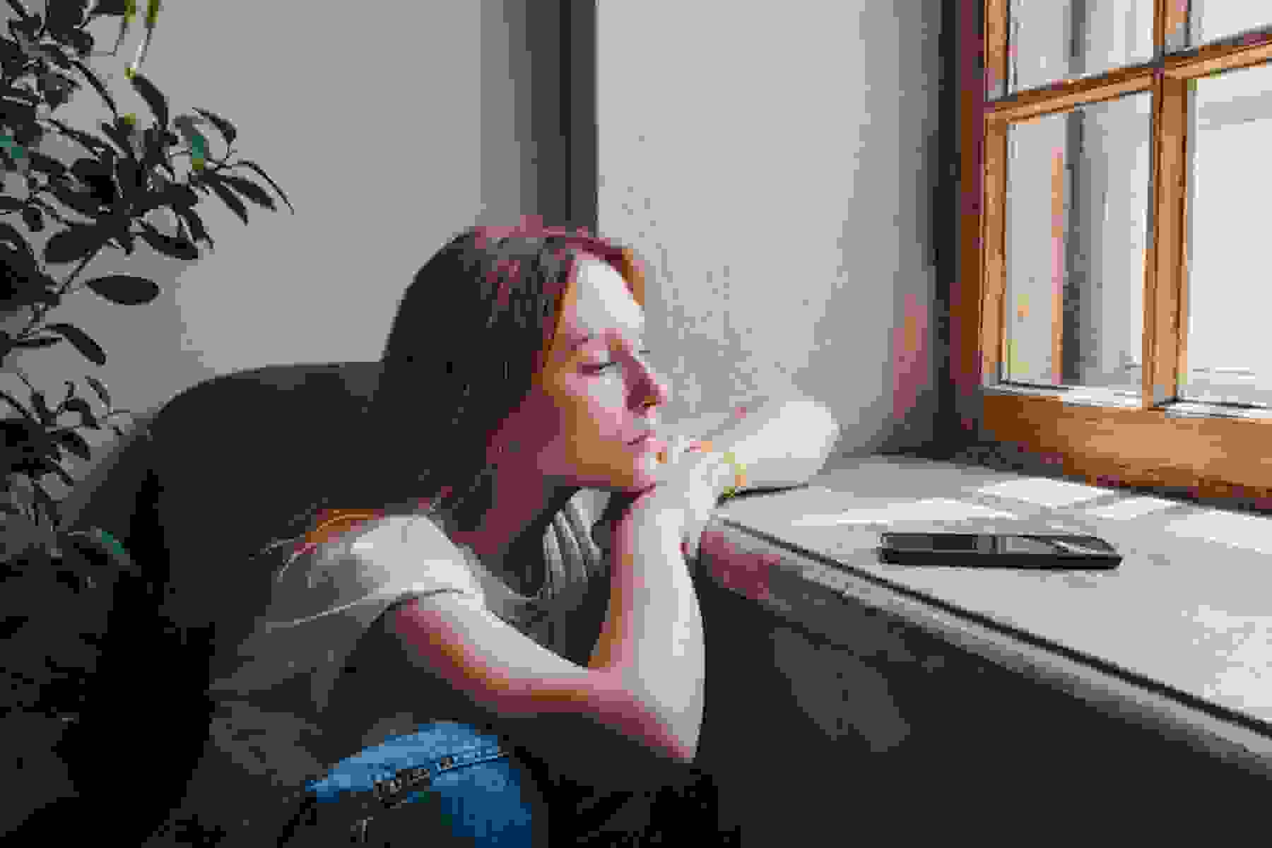 A woman sits forlornly at a window.