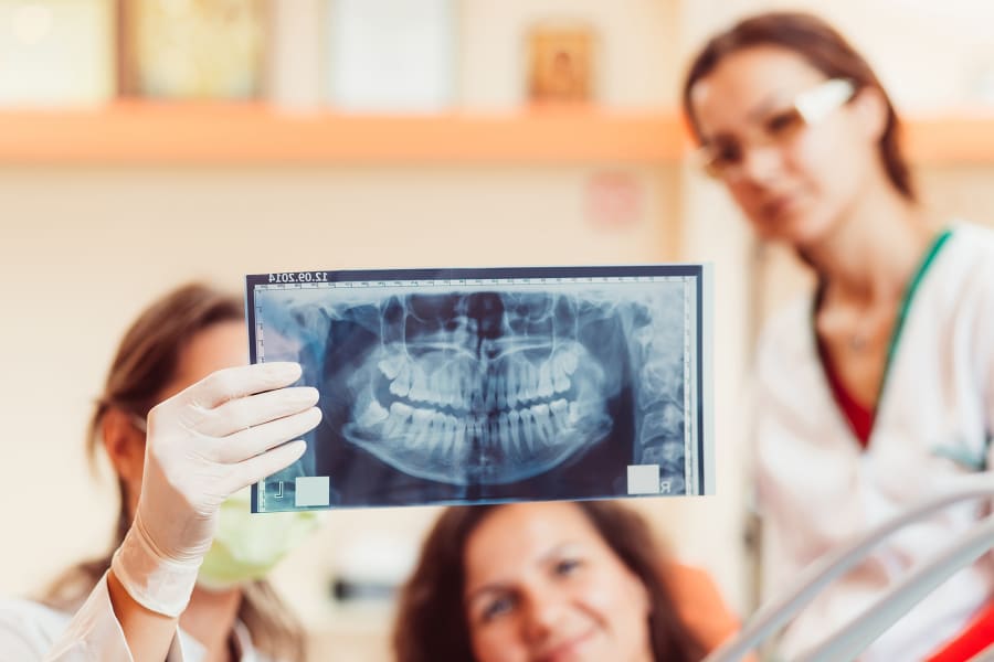 Two dentists and a patient look at an x-ray image of a woman's mouth.