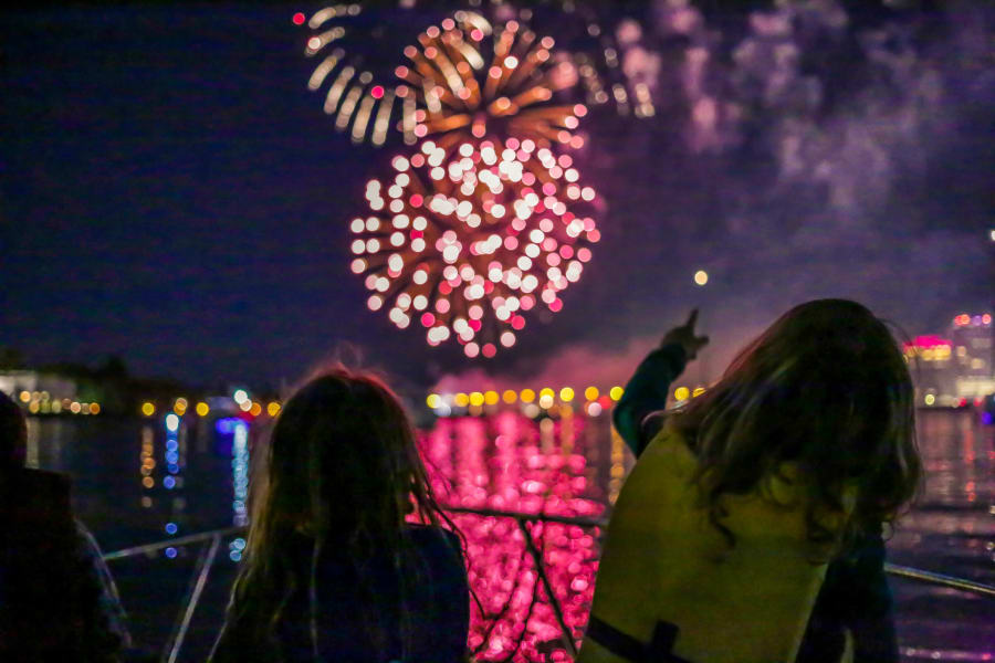 Kids in life jackets watch fireworks over the water.