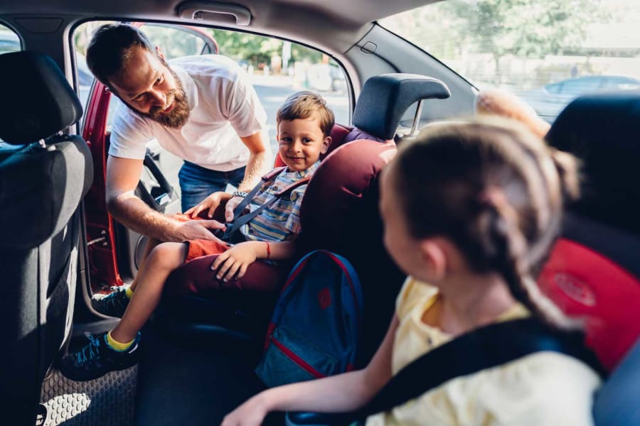 A father puts his kids into car seats.