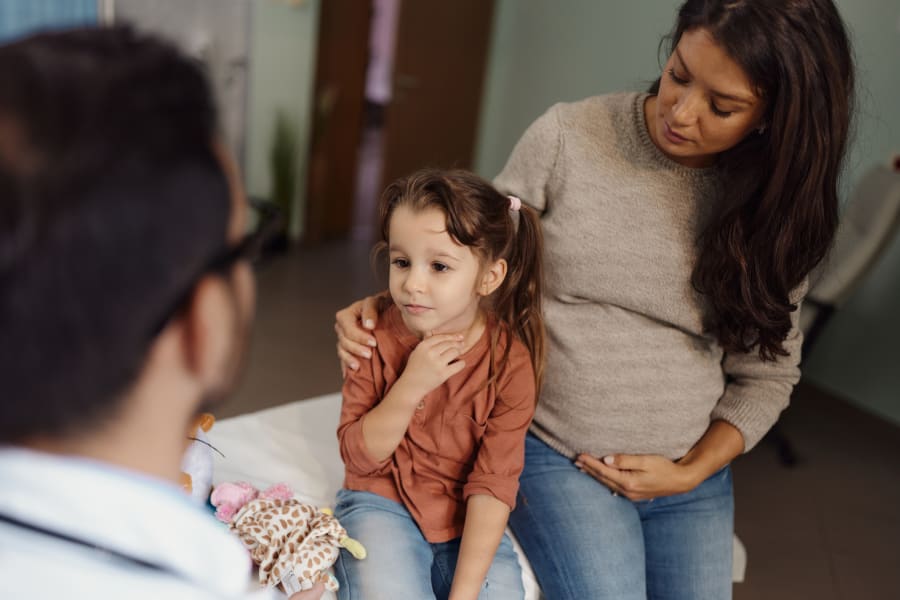 Small girl having a medical appointment with her pregnant mother at pediatricians'.
