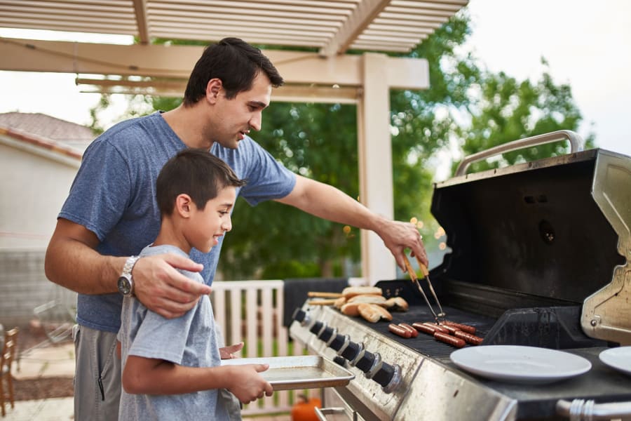 A father shows his son how to grill hot dogs.